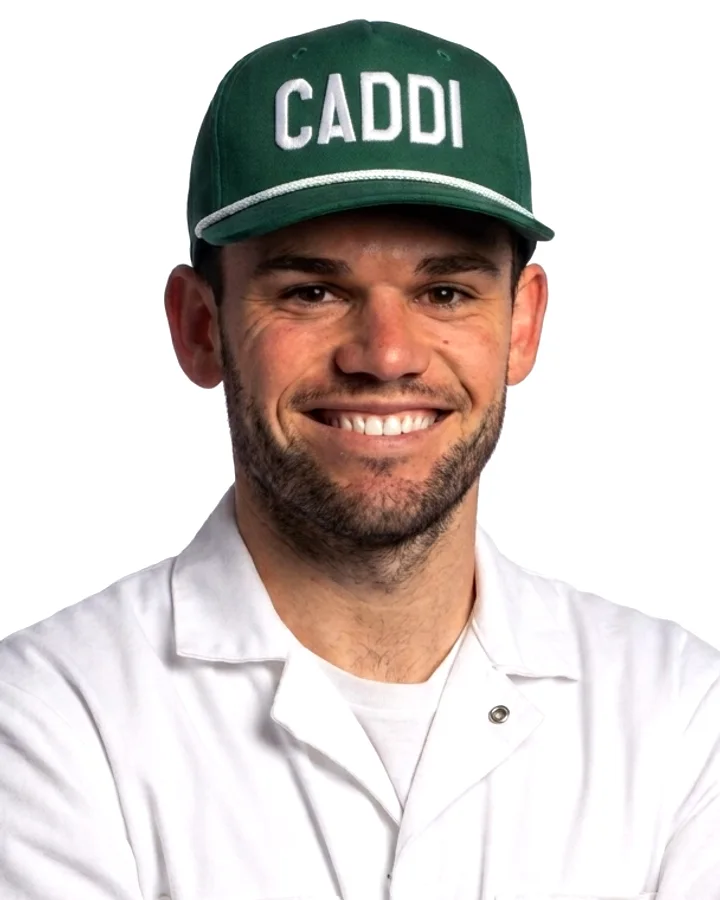 Caddi crew member in the white caddie uniform and green CADDI cap, smiling with arms crossed